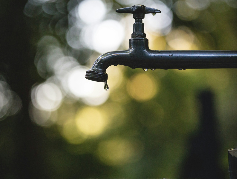 Tilt-shift lens photograph of a black steel faucet highlighting water age and how plumbing systems influence water quality over time, by Luis Tosta.