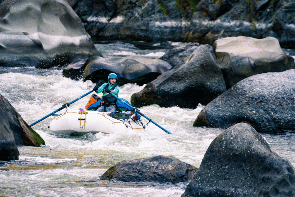 Kayaker navigating Blossom Bar rapid on the Rogue River, surrounded by rocks, representing river sports culture, photographed by Ben Kitching