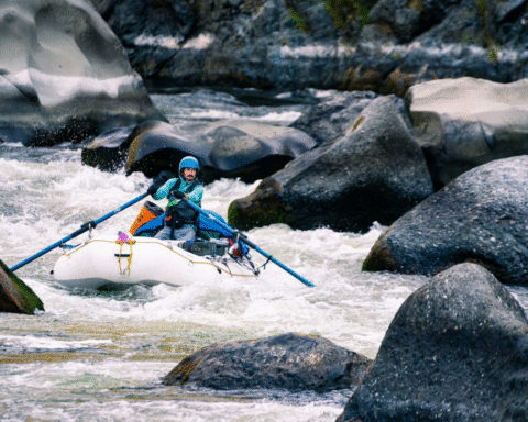 Kayaker navigating Blossom Bar rapid on the Rogue River, surrounded by rocks, representing river sports culture, photographed by Ben Kitching