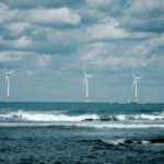 Sailboat on open sea with offshore wind turbines illustrating ocean energy and renewable coastal infrastructure