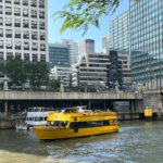 Yellow water taxis traveling down a river beside tall city buildings, illustrating urban waterfront transport and modern water taxis.