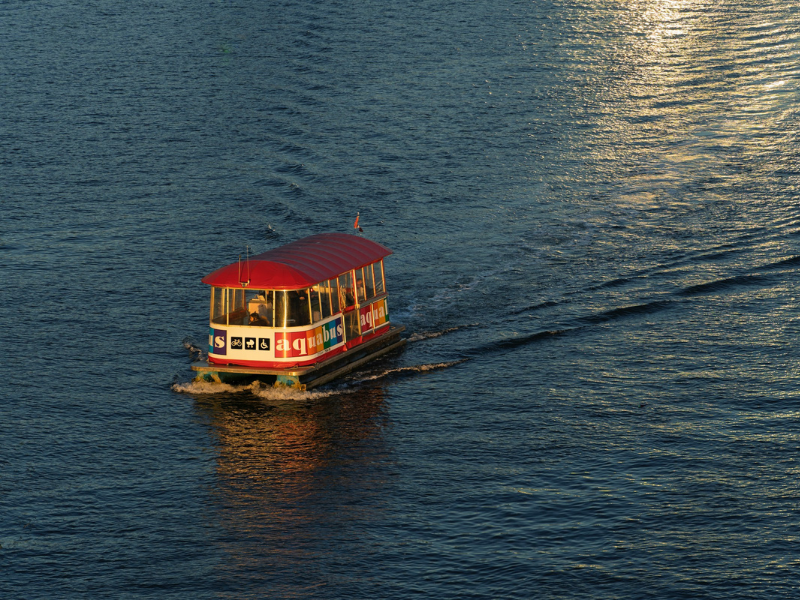 Red and white boat sailing on dark blue water, representing water taxis operating across coastal and urban waterways for passenger transport.
