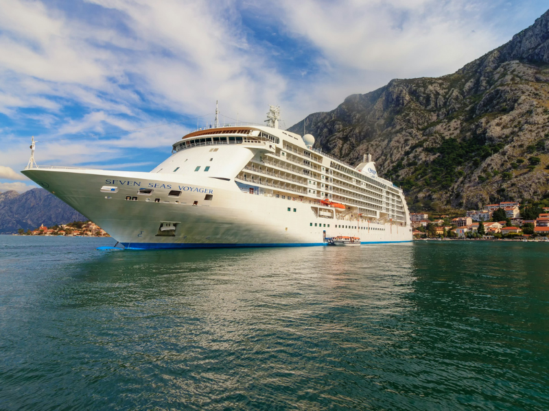 A river cruise ship sailing through calm waters with mountains rising in the background, showcasing scenic landscapes often experienced on river cruise journeys