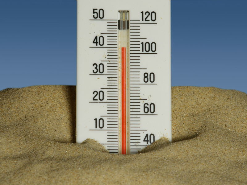 How Long Can You Survive Without Water? A thermometer placed in hot sand under a blue sky, illustrating how extreme heat increases dehydration risk.