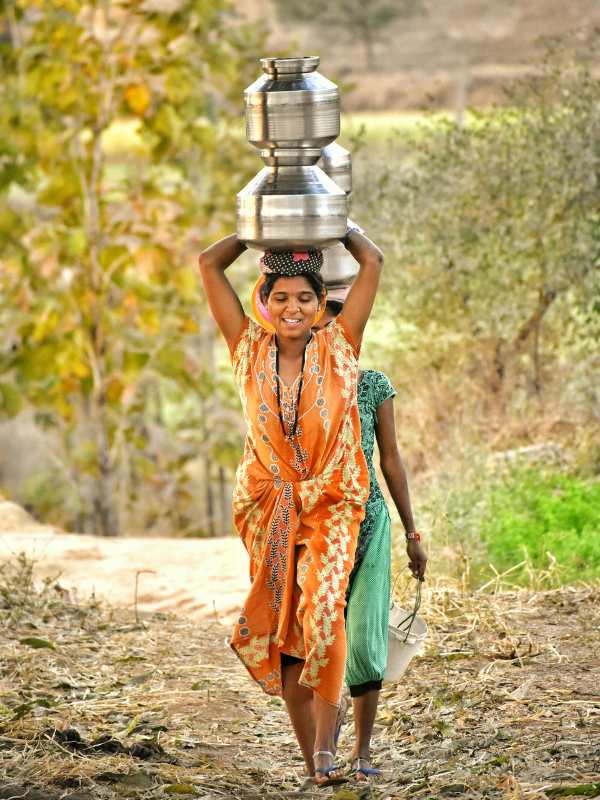 Woman carrying a water pot on her head along a dirt road, reflecting water access challenges on World Water Day 2026