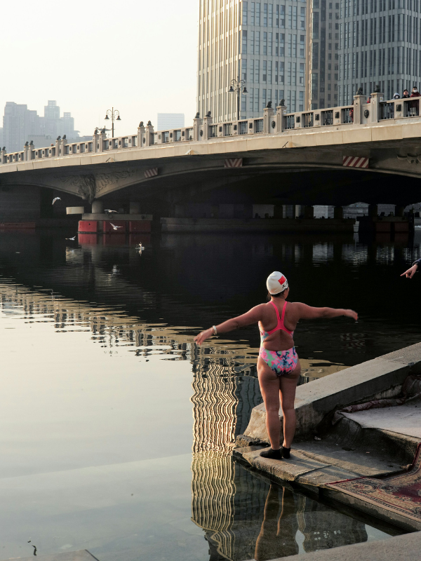 Woman in a bathing suit standing on a dock beside calm water before open water swimming