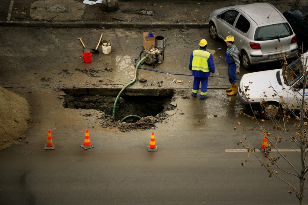 Workers repair a flooded underground drainage system on a city street, highlighting the growing importance of stormwater infrastructure and climate-resilient urban design.