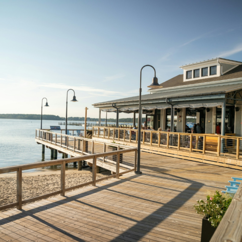 Wooden boardwalk and waterfront building beside a calm tidal park, showcasing a coastal space designed to adapt to changing tides and reconnect people with nature.