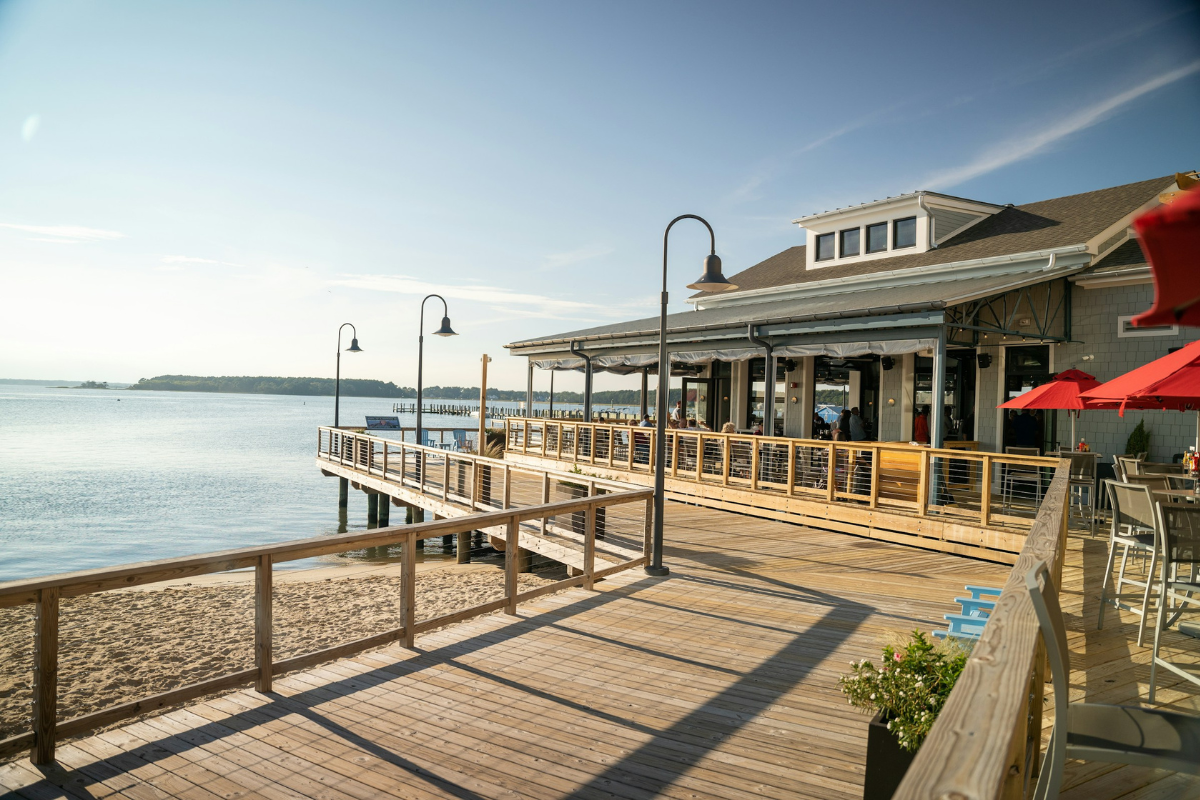 Wooden boardwalk and waterfront building beside a calm tidal park, showcasing a coastal space designed to adapt to changing tides and reconnect people with nature.