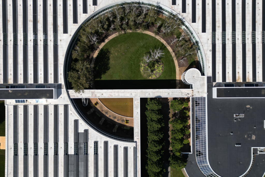 Aerial view of a modern building featuring a circular blue-green roof with lush vegetation, trees, and open green space integrated into the rooftop design.Blue-green roofs transform urban rooftops into living landscapes, managing stormwater while creating greener, more resilient cities.