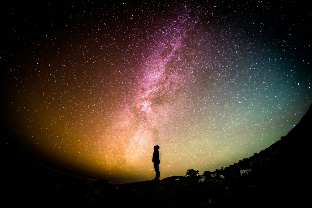 Silhouette of a person standing beside a coastal water landscape under the Milky Way, representing water-based night time tourism and stargazing.