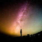 Silhouette of a person standing beside a coastal water landscape under the Milky Way, representing water-based night time tourism and stargazing.