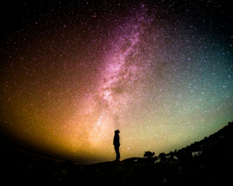 Silhouette of a person standing beside a coastal water landscape under the Milky Way, representing water-based night time tourism and stargazing.