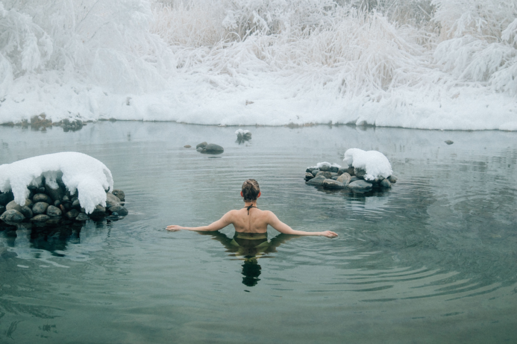 Person enjoying a cold water immersion in a snowy natural pool as part of a winter wellness ritual.