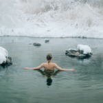 Person enjoying a cold water immersion in a snowy natural pool as part of a winter wellness ritual.