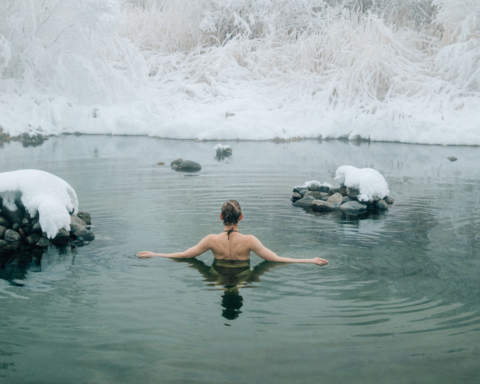 Person enjoying a cold water immersion in a snowy natural pool as part of a winter wellness ritual.