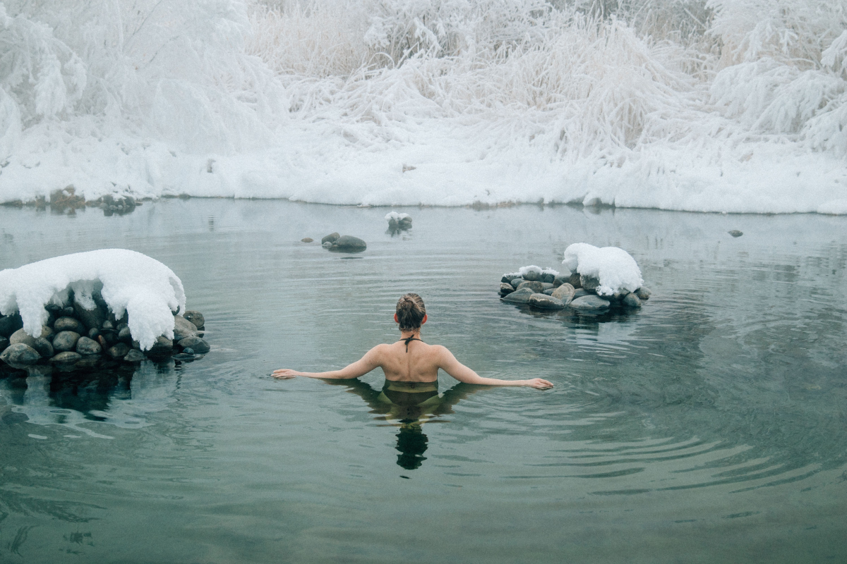 Person enjoying a cold water immersion in a snowy natural pool as part of a winter wellness ritual.