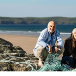 Ecotribo founders beside reclaimed fishing nets on a coastline, highlighting how recycled ocean plastic supports coastal communities, local manufacturing, and ocean stewardship.