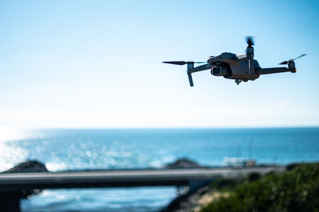 A drone flying above the ocean near a coastal bridge, demonstrating the use of drones for ocean observation, coastal monitoring, and marine research.
