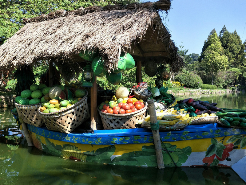 Traditional floating markets featuring a boat laden with fresh fruits and vegetables, showcasing water-based trade and local agriculture.