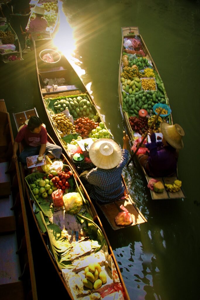 Floating markets with vendors selling fresh fruits and vegetables from traditional wooden boats along a busy waterway.