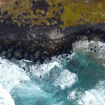 Aerial view of ocean waves meeting a rocky coastline, showing how the tide shapes the shores of coastal islands.