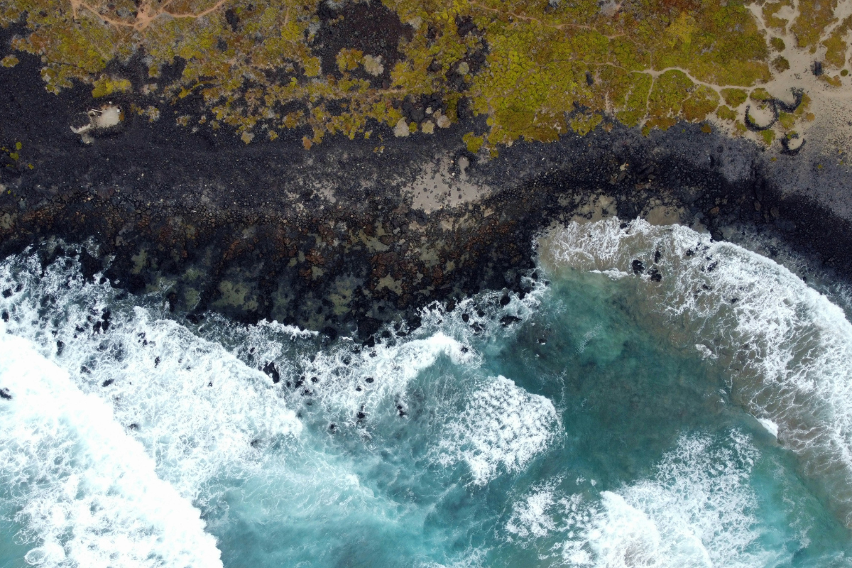 Aerial view of ocean waves meeting a rocky coastline, showing how the tide shapes the shores of coastal islands.