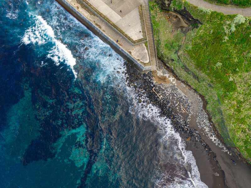 The tide meets a rugged coastline, where deep blue water, rocky shores and coastal infrastructure exist side by side.