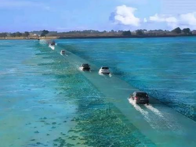 As the tide rises, a once-visible coastal road becomes submerged, transforming an ordinary drive into a journey through the sea.