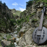 : Large string instrument beside a rocky mountain stream, representing the connection between music, nature and river soundscapes.