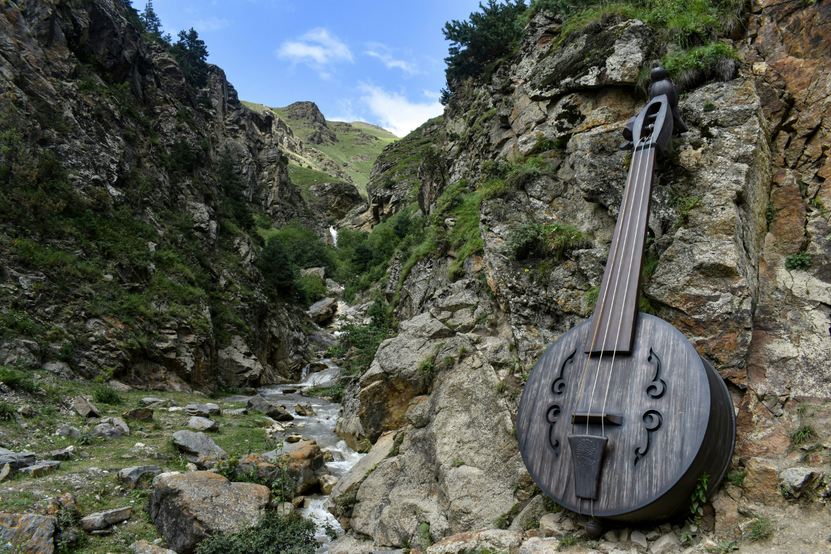 : Large string instrument beside a rocky mountain stream, representing the connection between music, nature and river soundscapes.