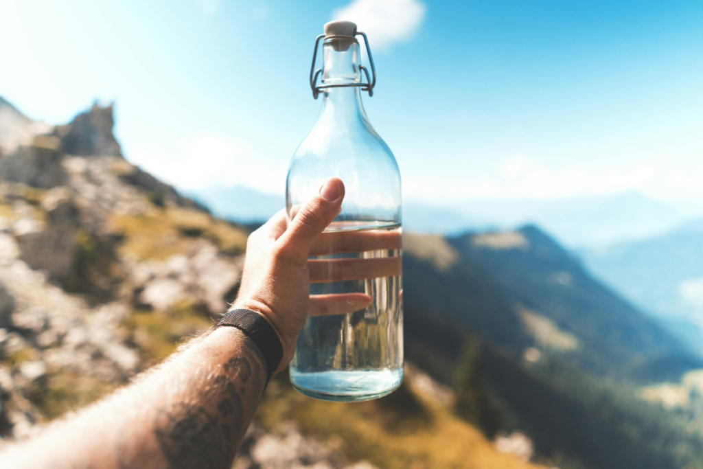 A traveller holds a glass water bottle against a mountain landscape, highlighting tourism water scarcity and the importance of freshwater conservation.