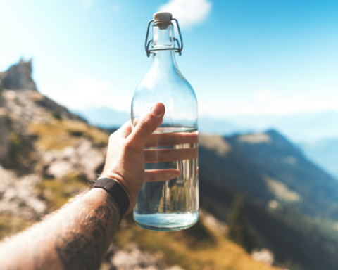 A traveller holds a glass water bottle against a mountain landscape, highlighting tourism water scarcity and the importance of freshwater conservation.